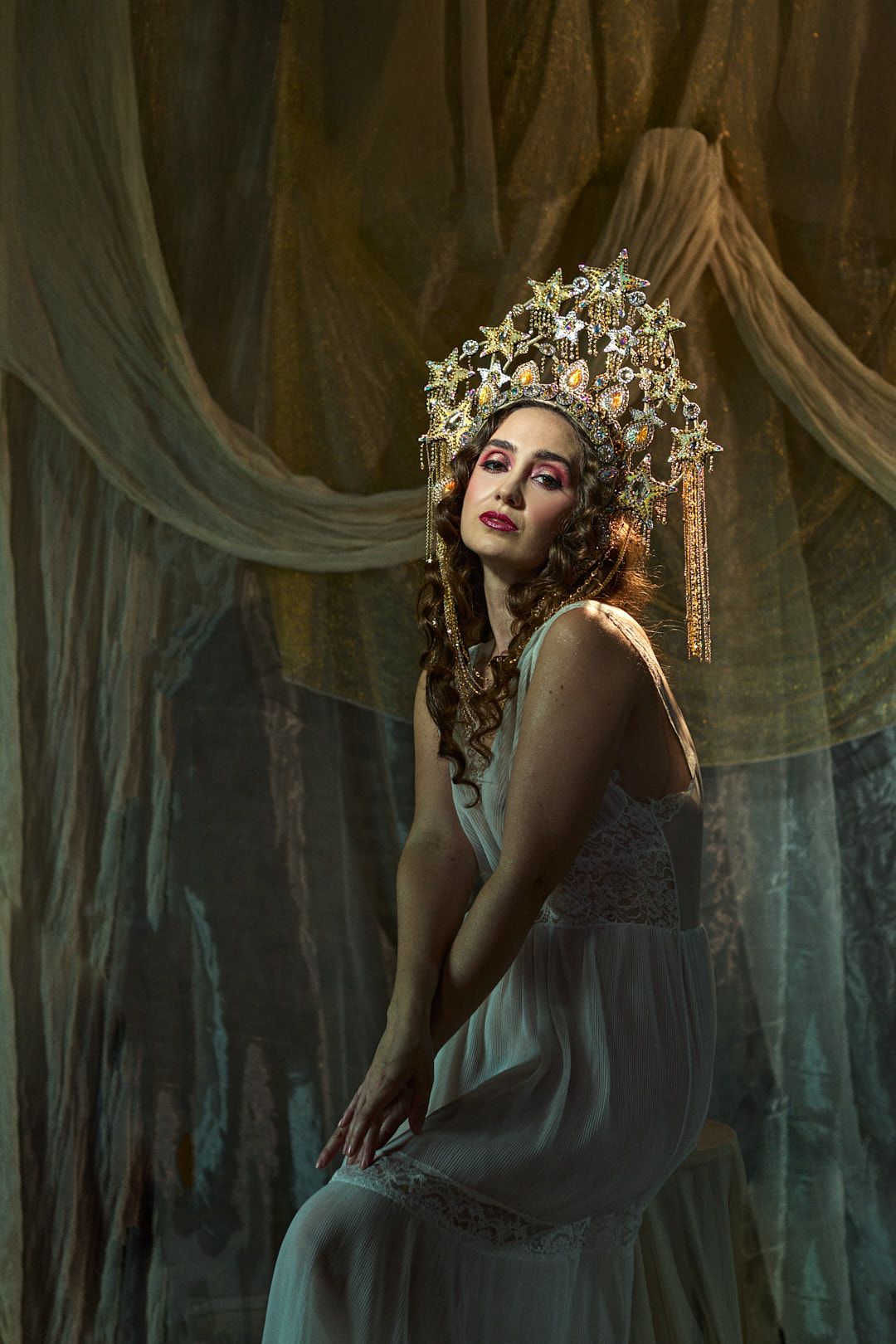 Ethereal portrait featuring an ornate golden crown and flowing sheer fabric in a dreamy atmospheric setting.