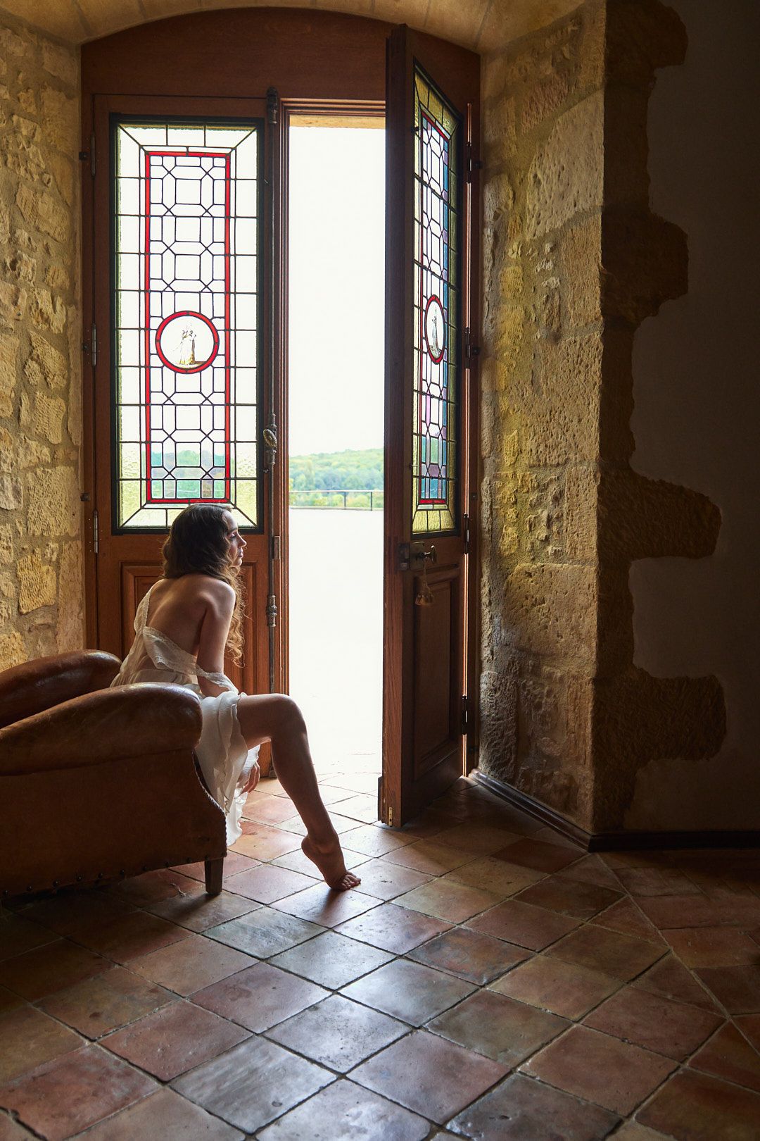 Interior of stone castle room with sunlight streaming through decorative windows onto terracotta floor tiles.