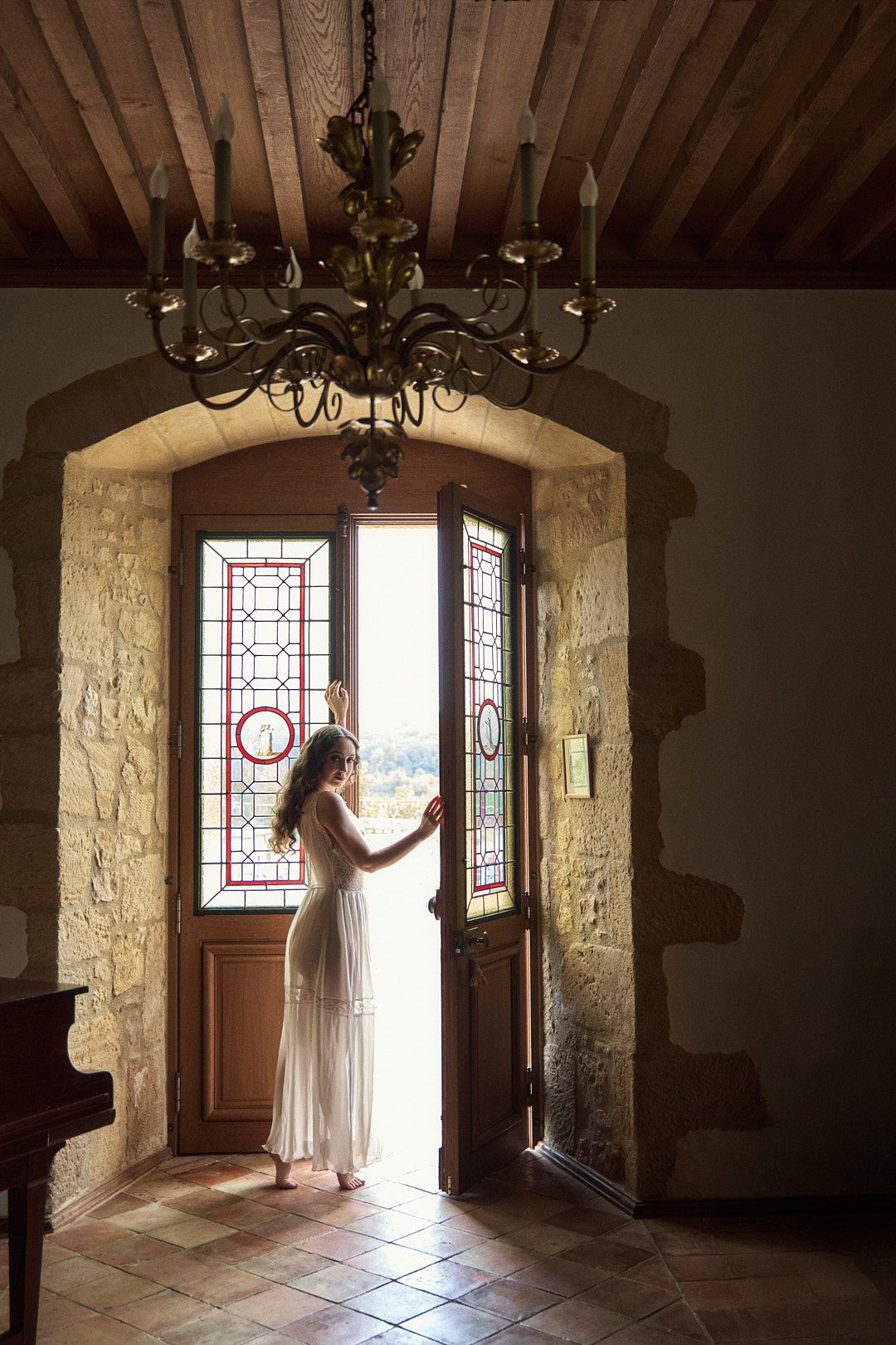 Figure in white dress standing in sunlit stone doorway of historic building.