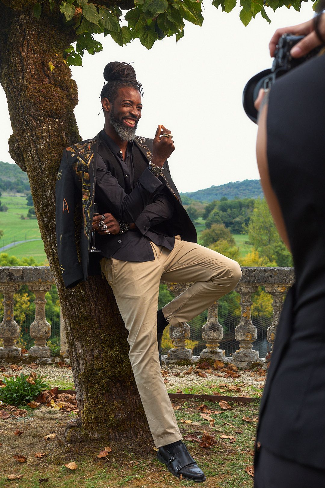 Playful outdoor photoshoot against stone wall with trees and countryside in background.