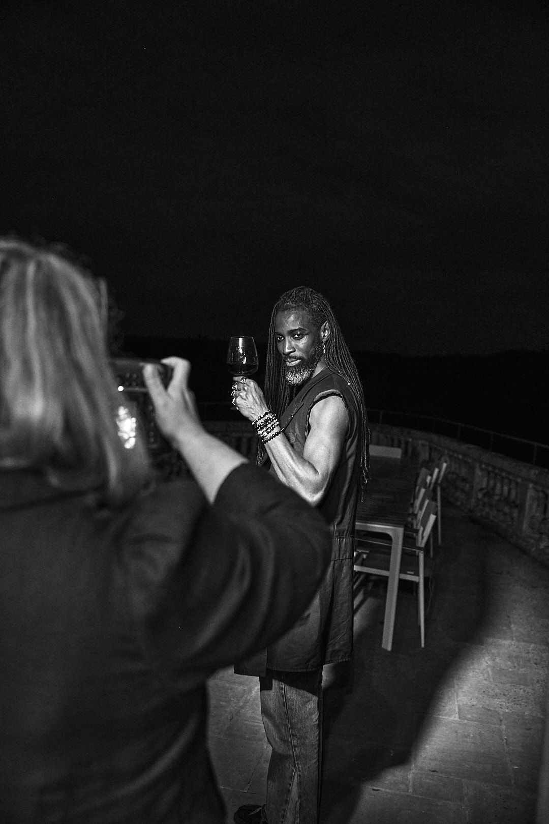 Black and white nighttime photo of someone being photographed while holding a bottle.