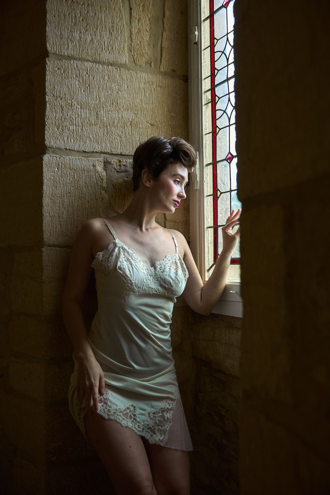 Artistic portrait of someone in white lingerie posing by a church window.