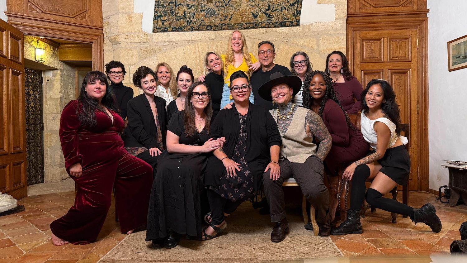 Large group photo of people sitting together in formal attire against wooden paneled wall.