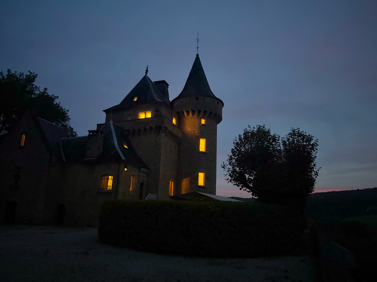 Castle with illuminated windows at twilight featuring distinctive turrets and towers.