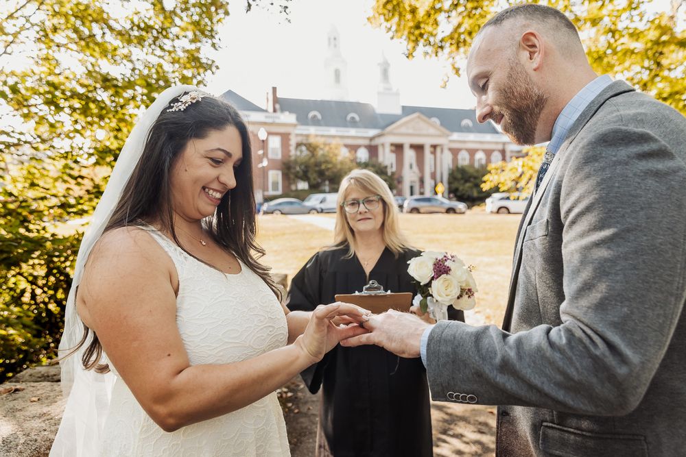 A couple holds hands during an autumn outdoor wedding ceremony with golden leaves in the background.
