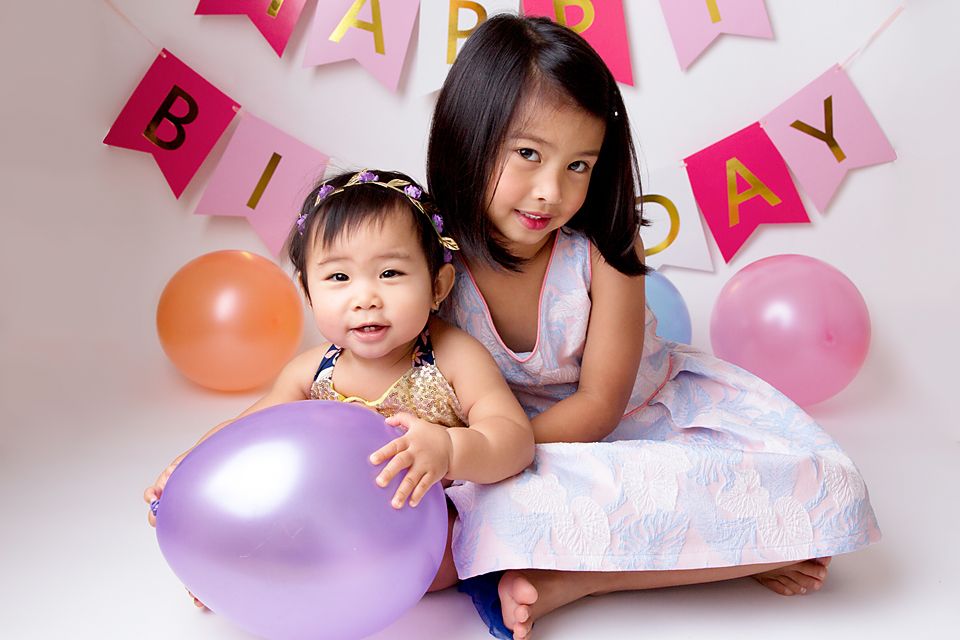 Happy family group lying on floor with pink and purple balloons during photo session.