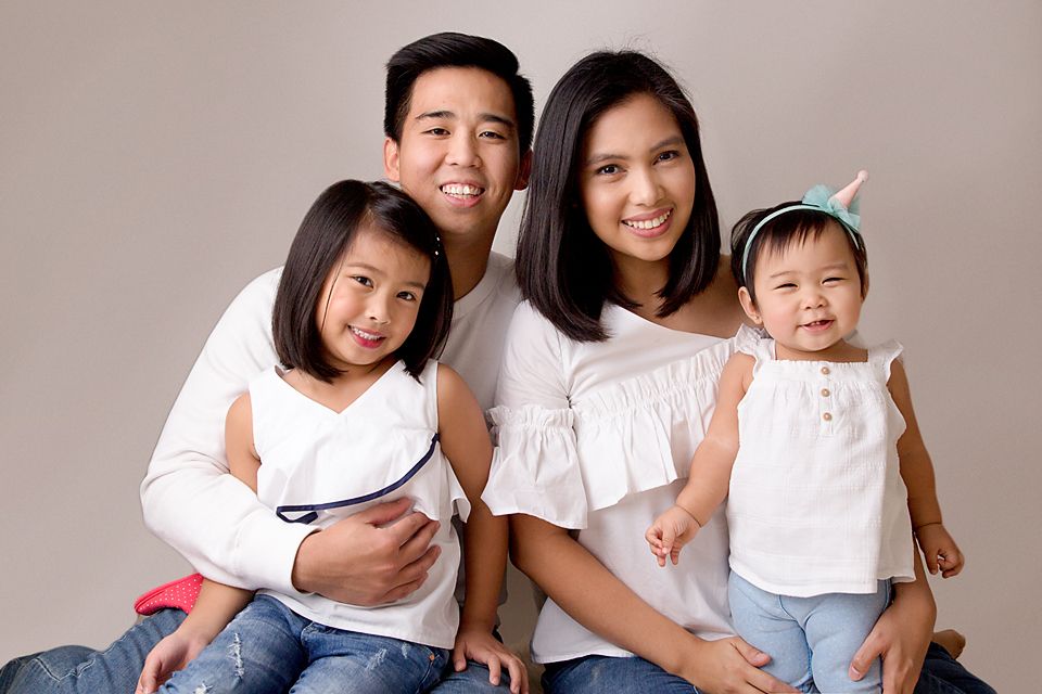 Family portrait session with everyone wearing white against neutral background.
