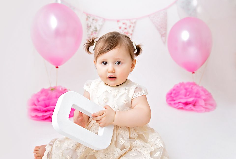 Birthday photoshoot with pink balloons, white lace dress and number one prop.