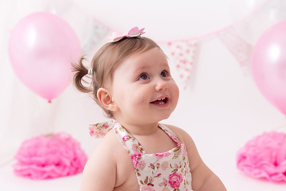 Pink birthday setup with floral dress, pink balloons and tissue paper decorations.