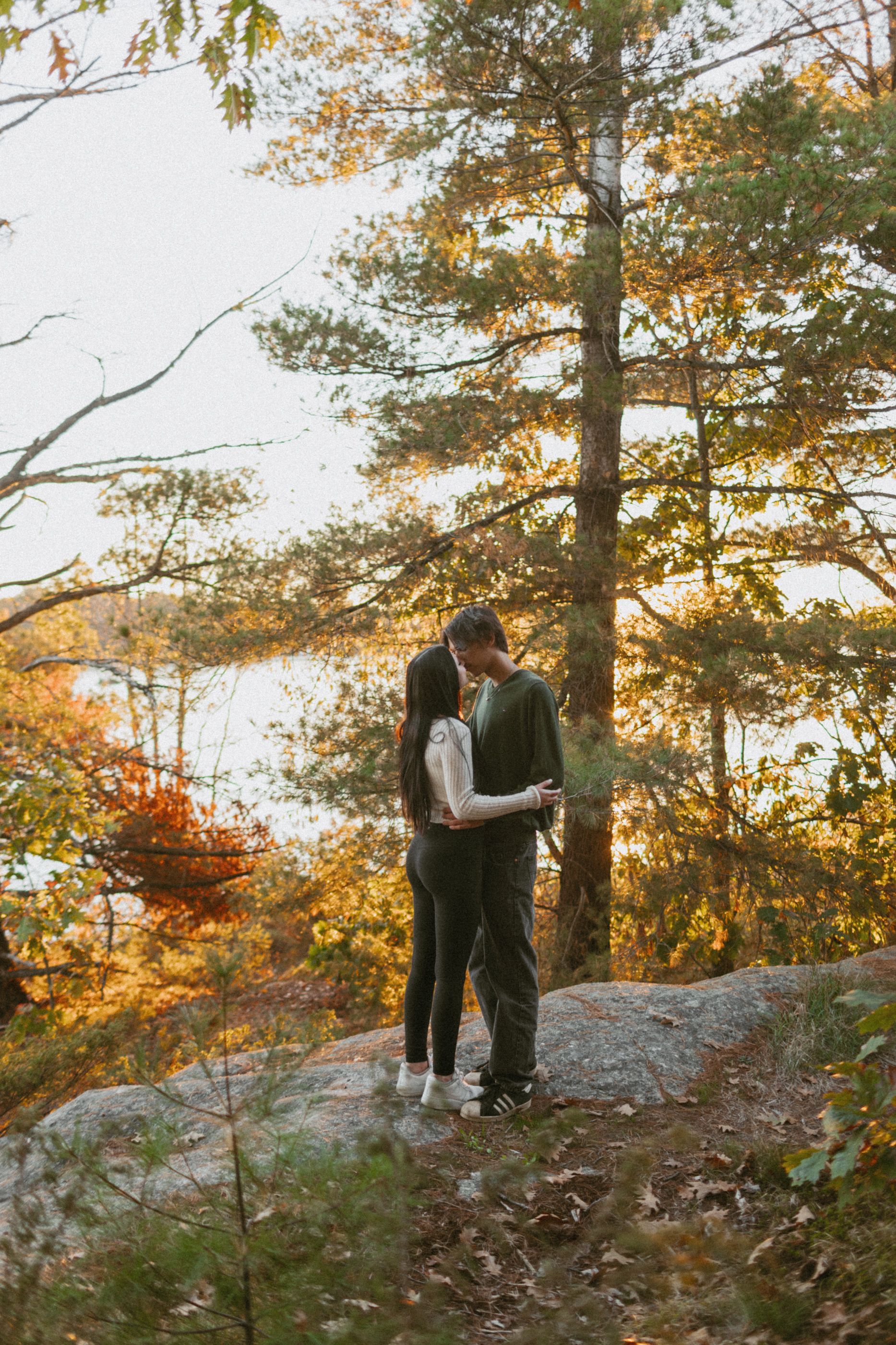 A couple stands among fall foliage on a rocky hillside during an autumn afternoon.
