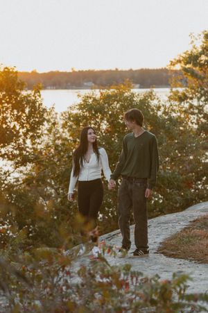 A couple walks together at sunset near a lake surrounded by autumn trees.