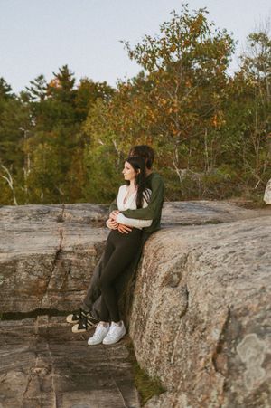 Couple sitting together on a rocky cliff edge surrounded by fall foliage.