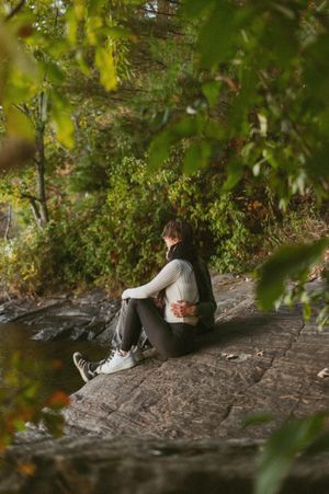 Couple relaxing on rocky terrain framed by green leaves in natural lighting.