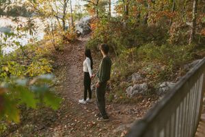 Couple walking along an autumn trail with fallen leaves and trees.