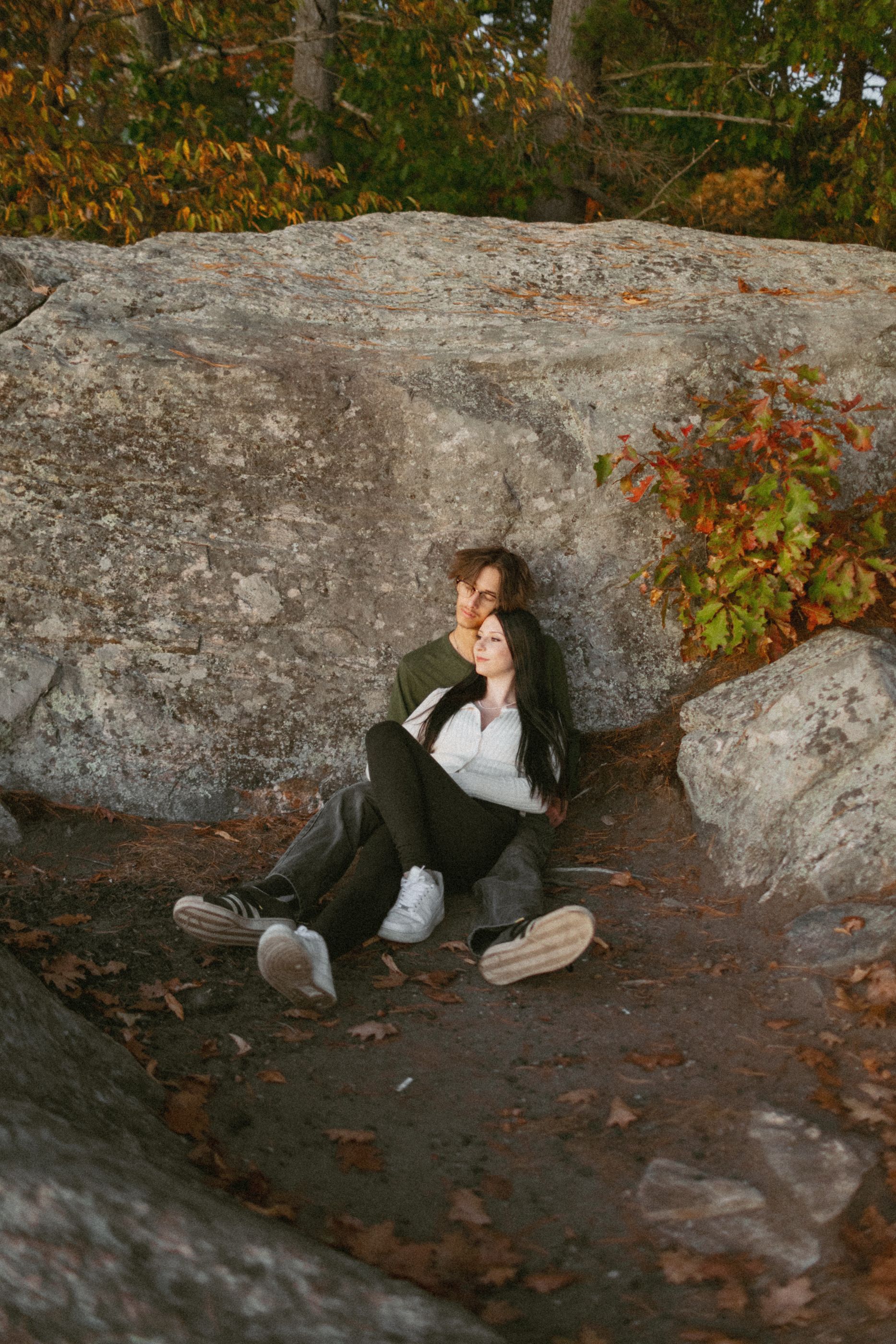 Couple resting against large rocks surrounded by fall foliage.