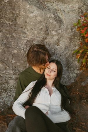 Intimate moment shared between couple against textured rock wall in autumn setting.