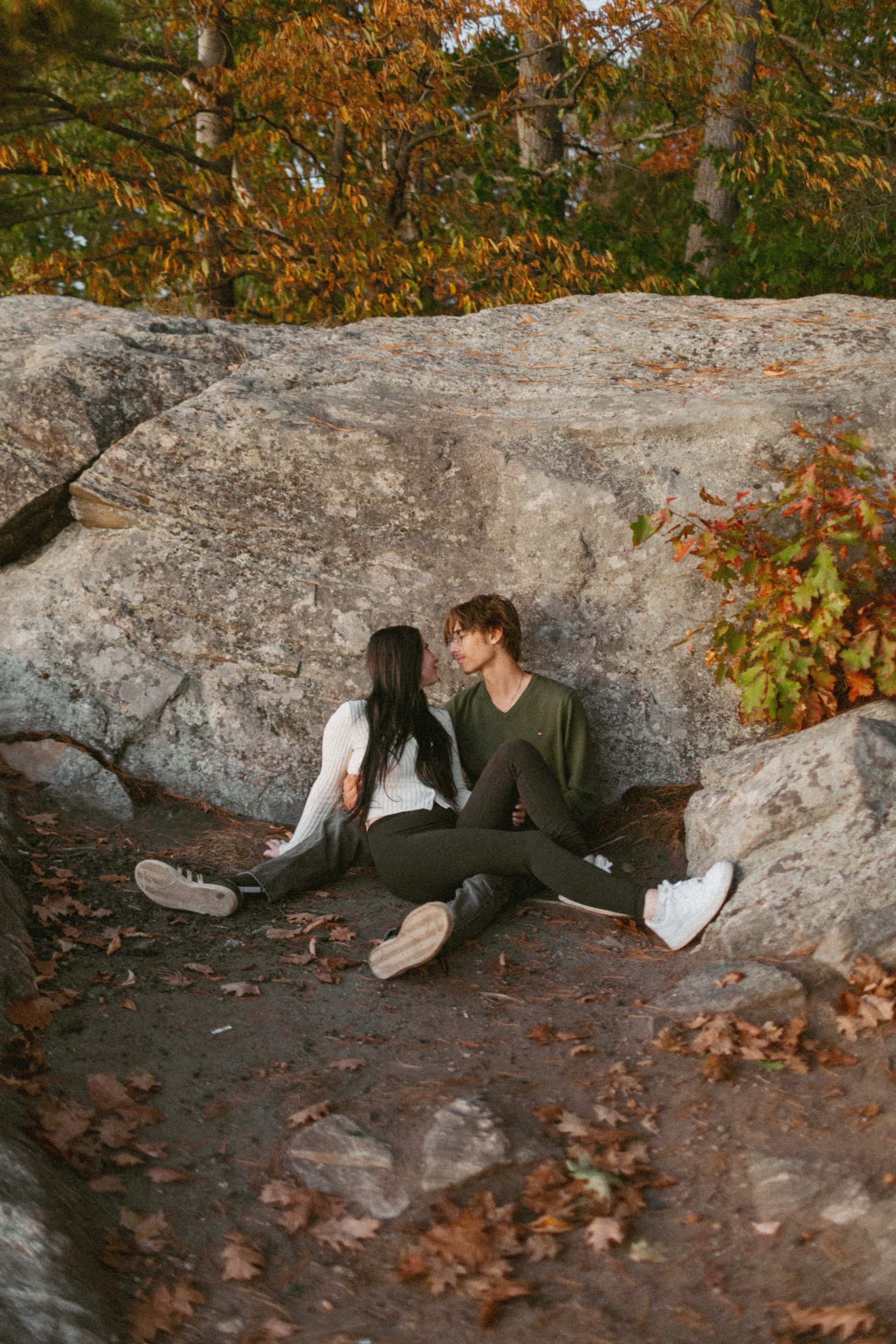 Couple lounging on rocky ground surrounded by autumn leaves.