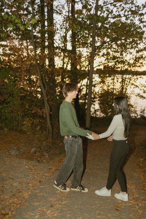 Playful couple walking through fallen leaves at sunset in a wooded area.