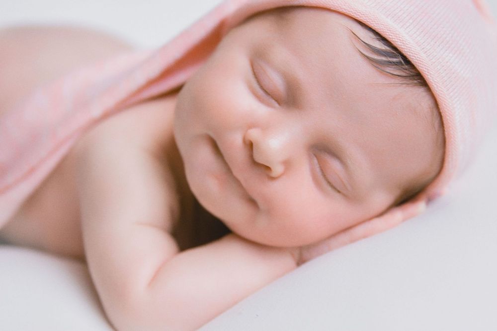 A sleeping newborn baby swaddled in soft pink blankets, captured in a series of peaceful close-up portraits.