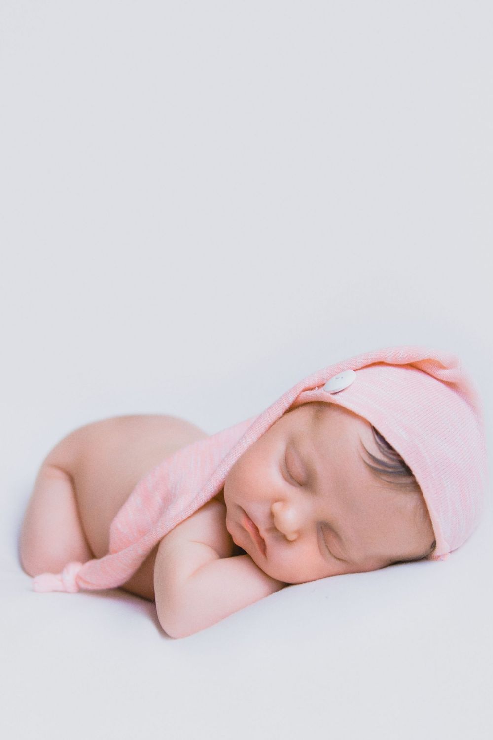 A sleeping baby in a pink hat lies peacefully on a white background in a series of four connected photos.