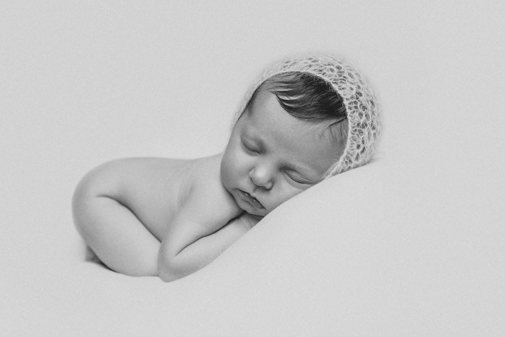 A series of black and white photographs showing a sleeping newborn baby in various peaceful poses.