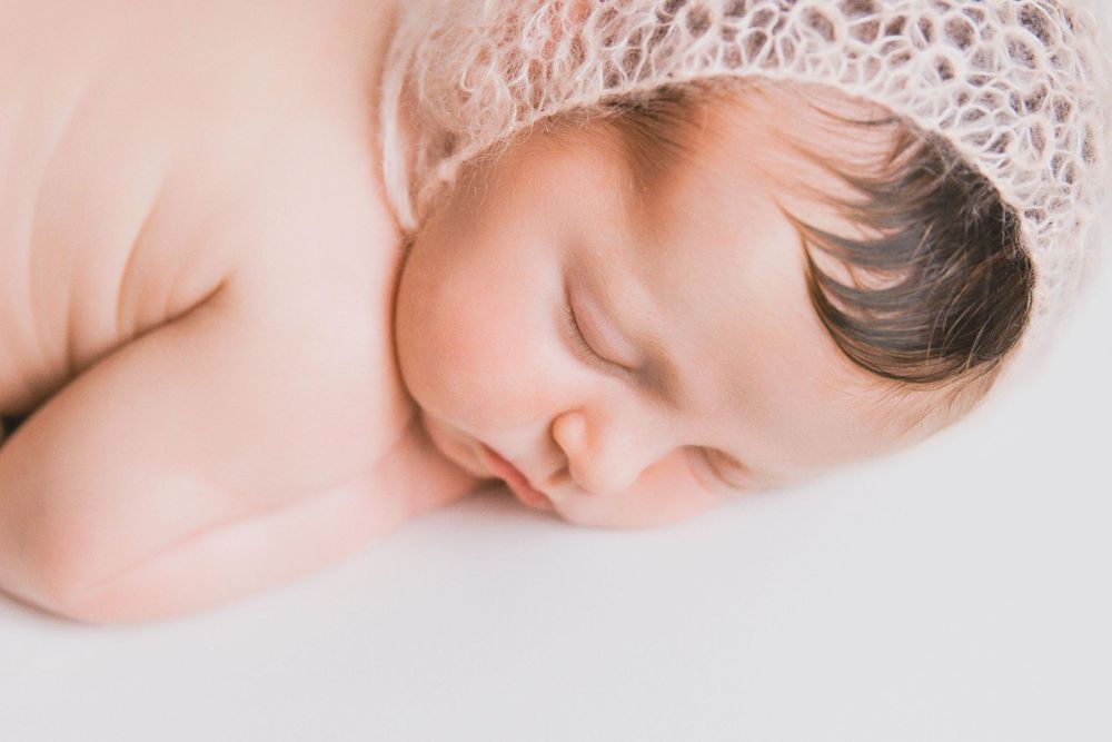 Sweet newborn baby sleeping peacefully on soft white blanket during professional photo session.