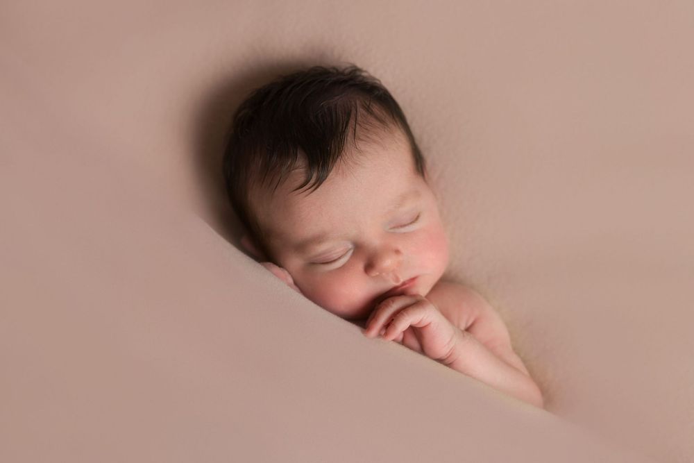 Sleeping newborn posed on soft brown background during studio portrait session.