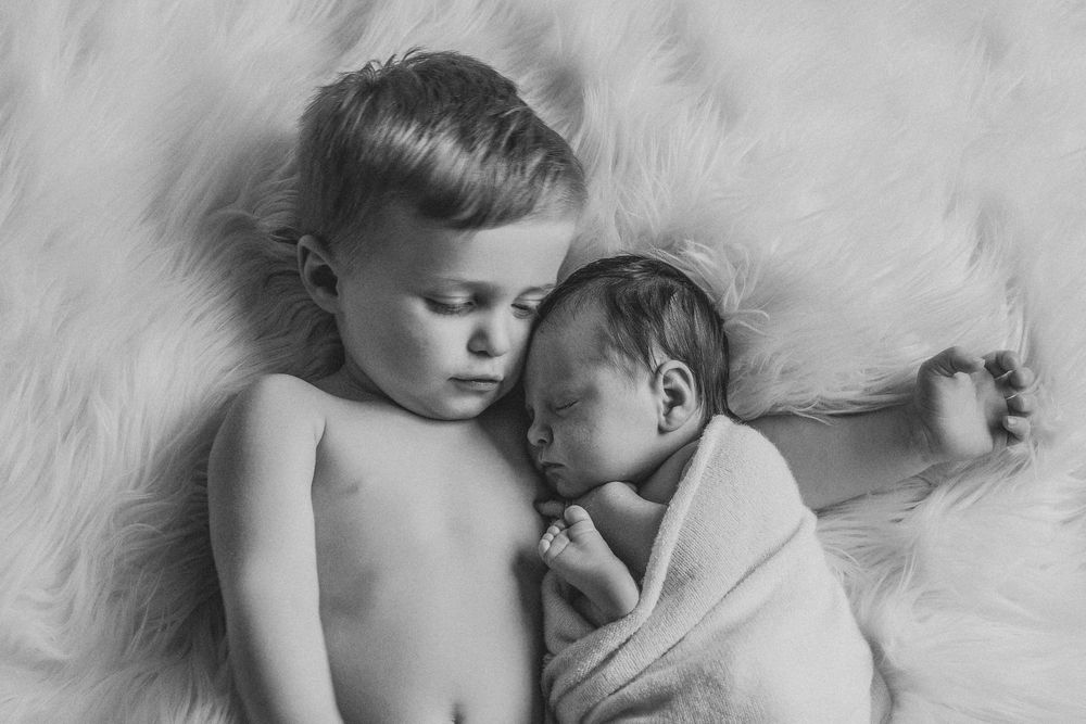 Black and white portrait of two siblings lying together on soft furry blanket.