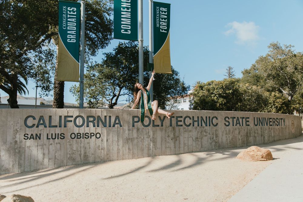 California Polytechnic State University San Luis Obispo sign with graduation banners on sunny campus.