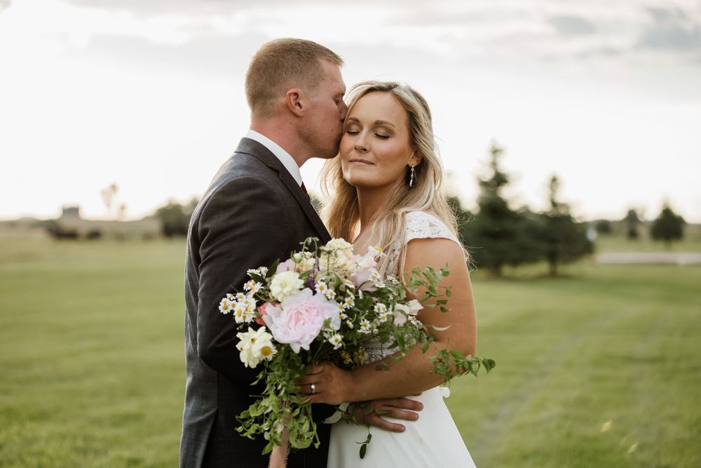 A couple embraces in a scenic meadow with mountains in the background.