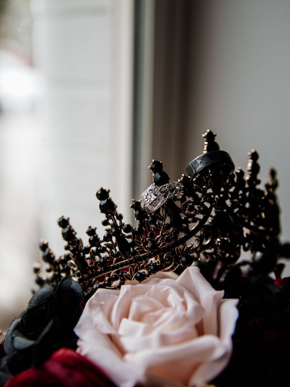 Ornate black crown with delicate details next to pink rose in dramatic lighting.