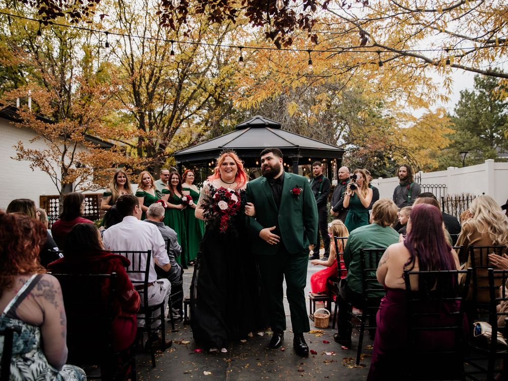 Outdoor autumn wedding celebration under gazebo with guests in green and black attire.