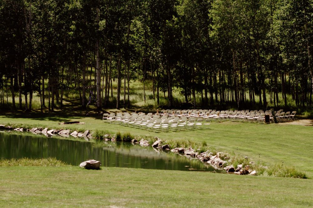 Panoramic view of an outdoor wedding ceremony setup with wooden chairs in a forest setting.