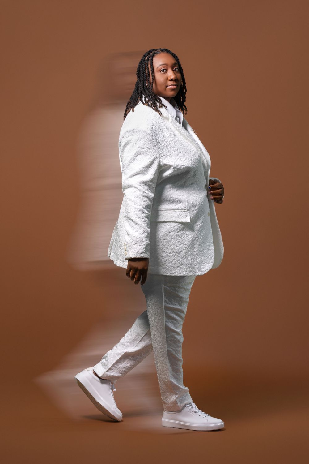 Fashion portrait of person in all-white ensemble against brown background.