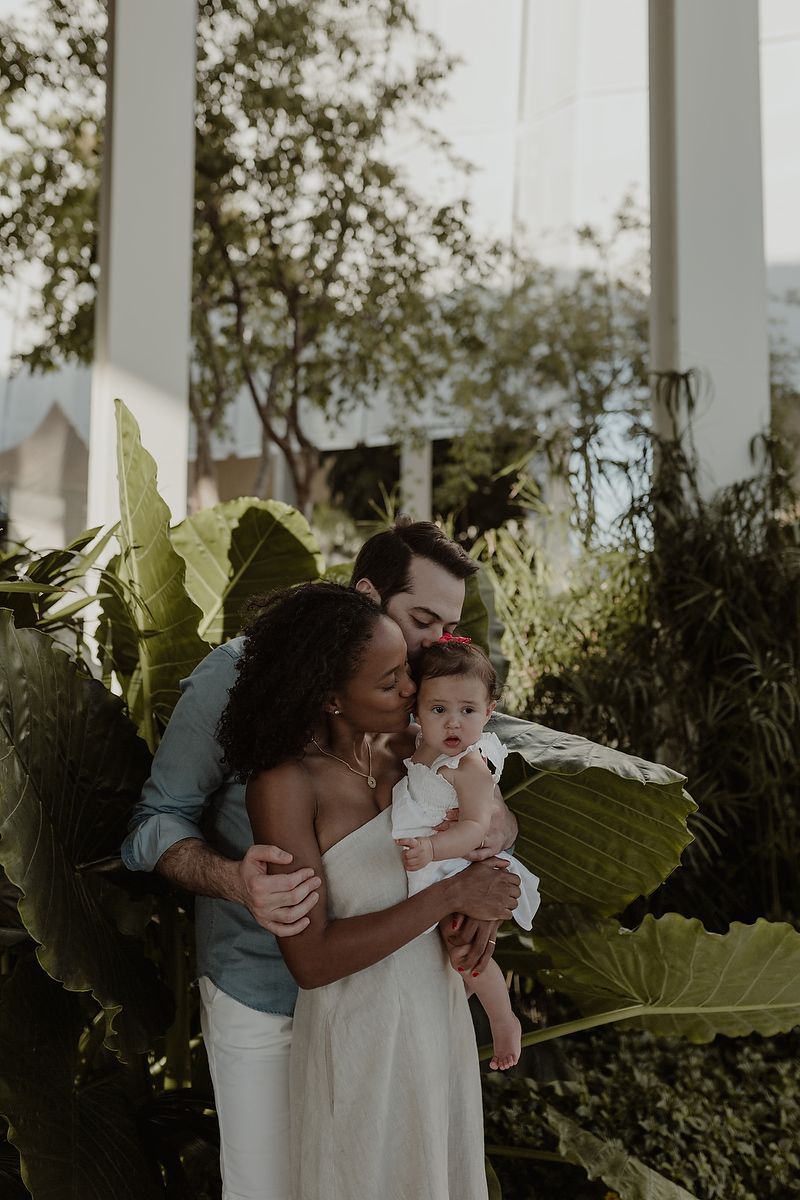Parents embracing with daughter in tropical garden at Playa del Carmen destination family photoshoot.