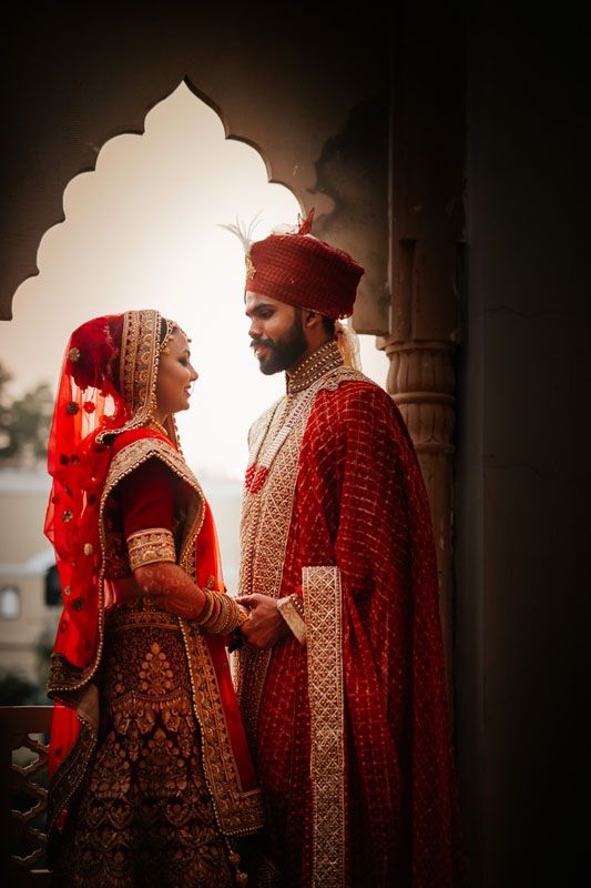 A romantic wedding portrait of a couple in traditional red Indian wedding attire framed by architectural elements.