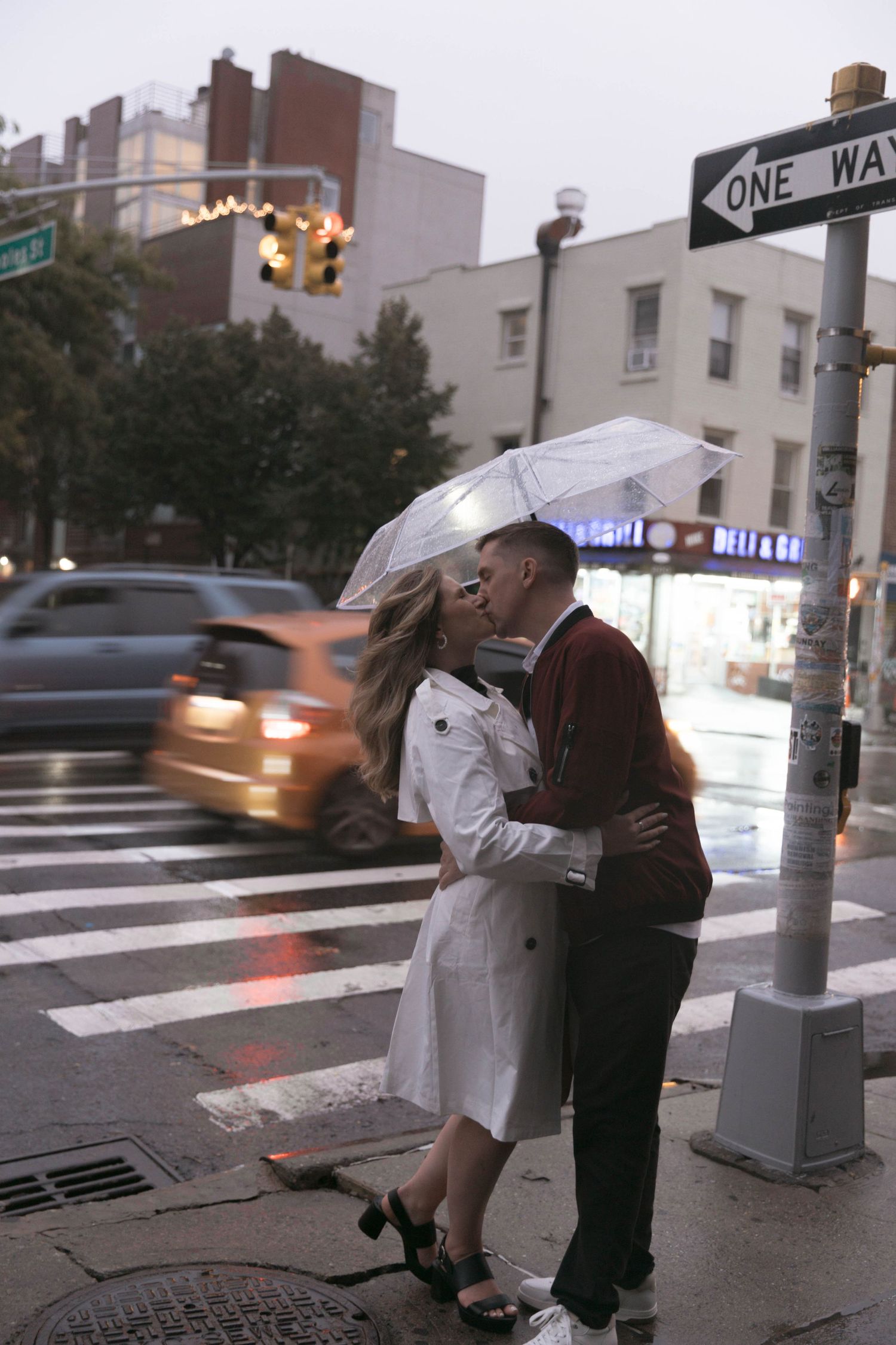 A couple shares a romantic moment under an umbrella on a rainy city street corner.