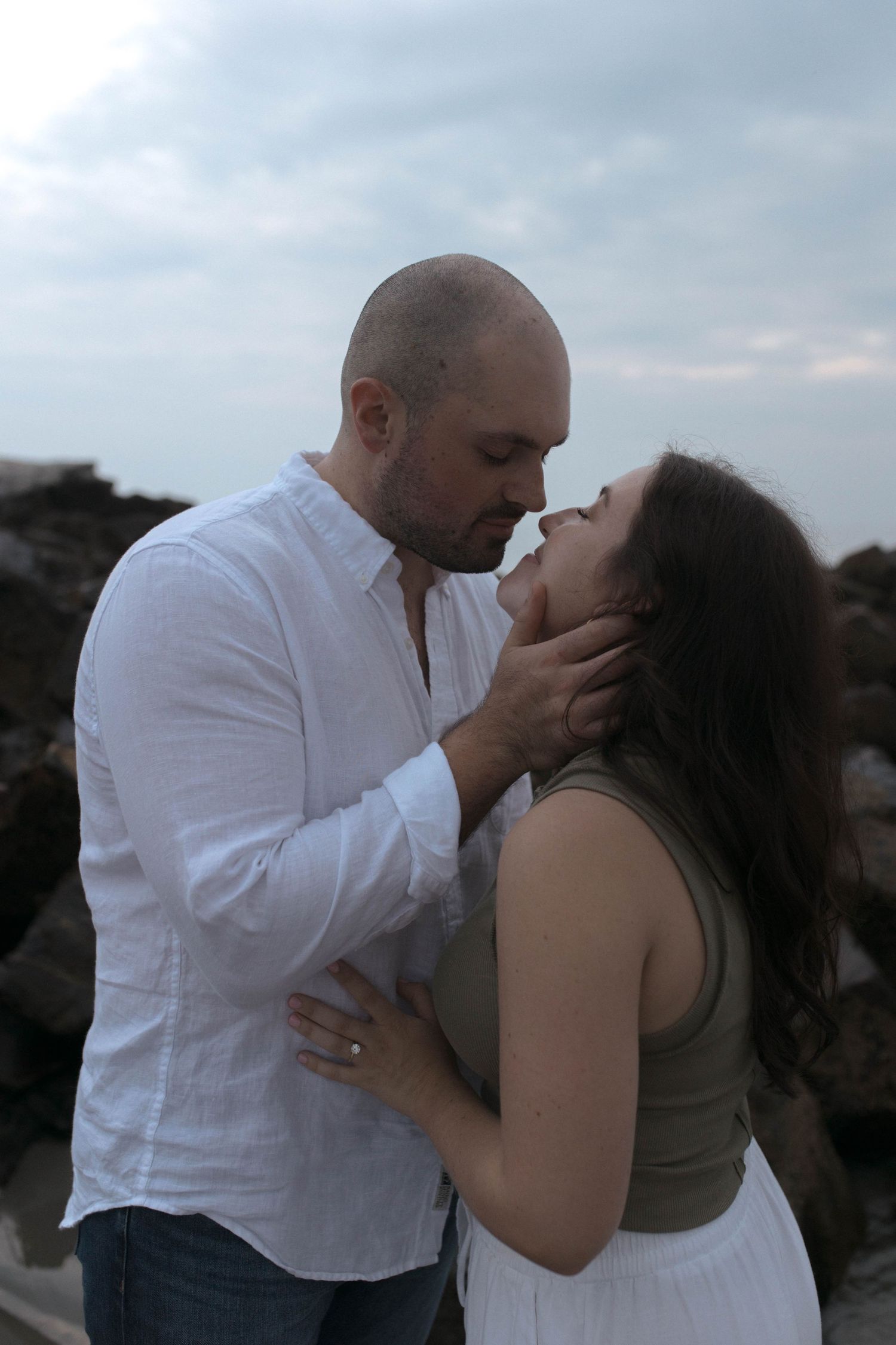 Romantic couple sharing intimate moment on rocky beach during sunset.
