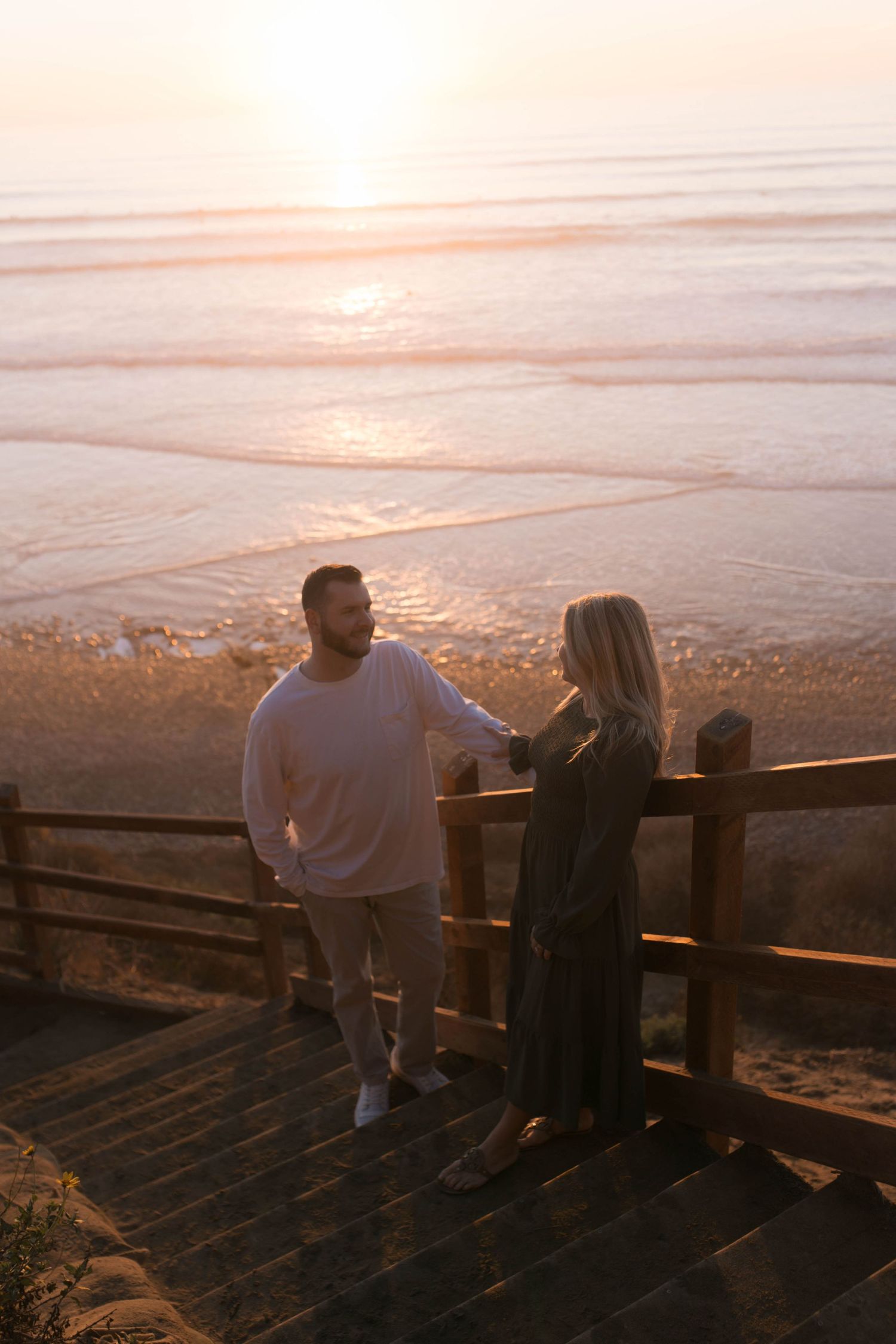 Couple enjoying scenic sunset view from wooden observation deck overlooking misty rolling hills and distant horizon.
