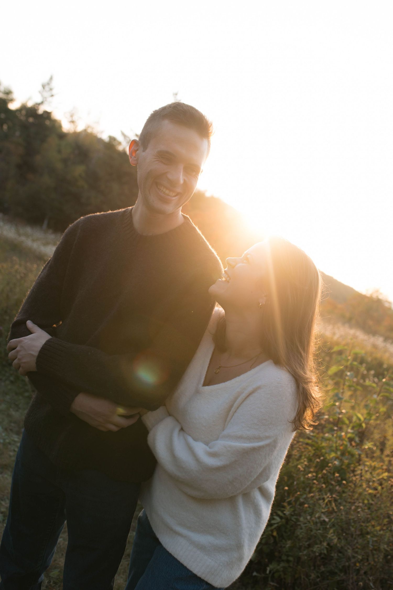 A couple shares a candid moment together outdoors during golden hour sunset with natural lens flare.