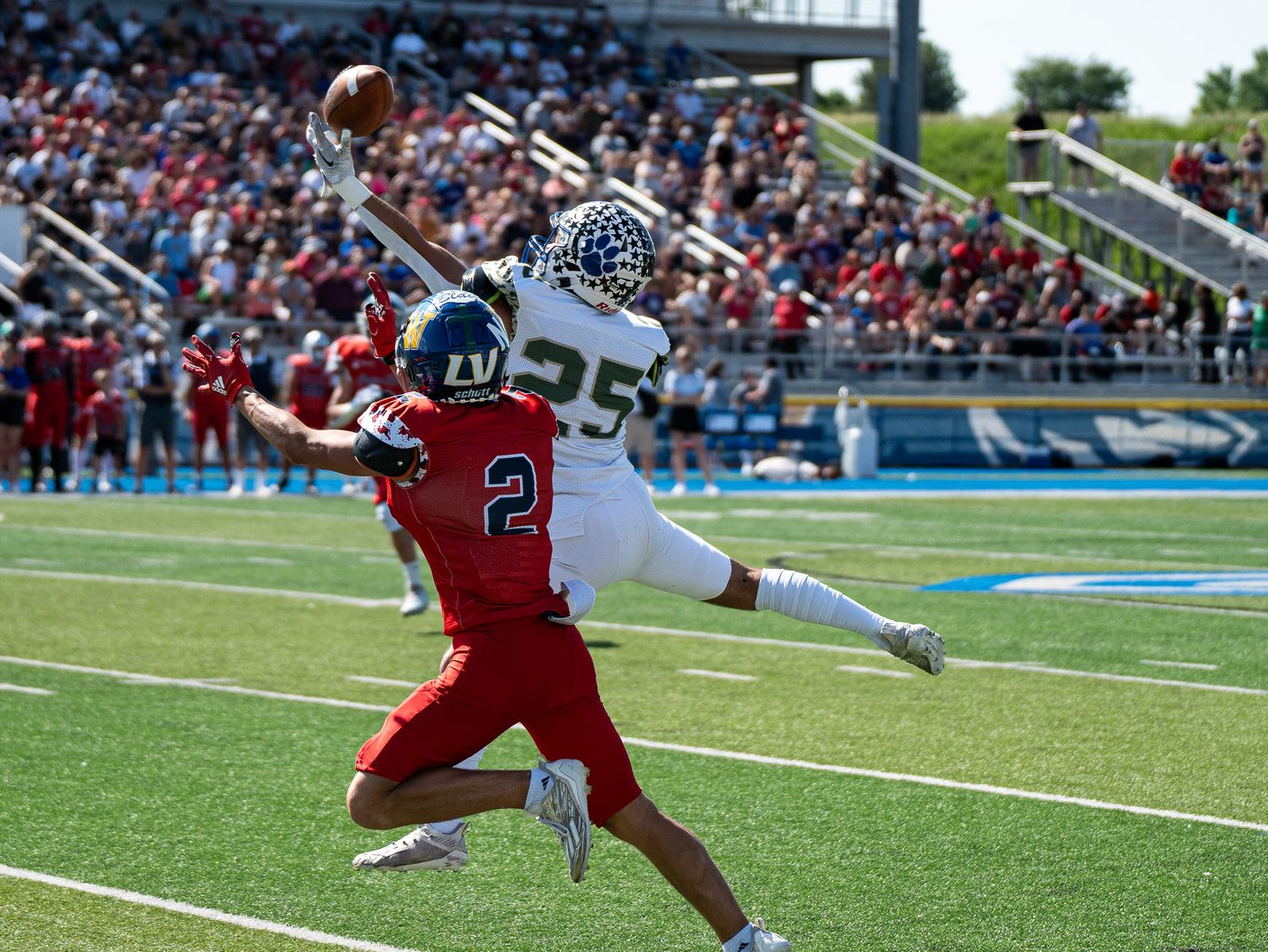 Two players jump high to compete for a football pass during a game.