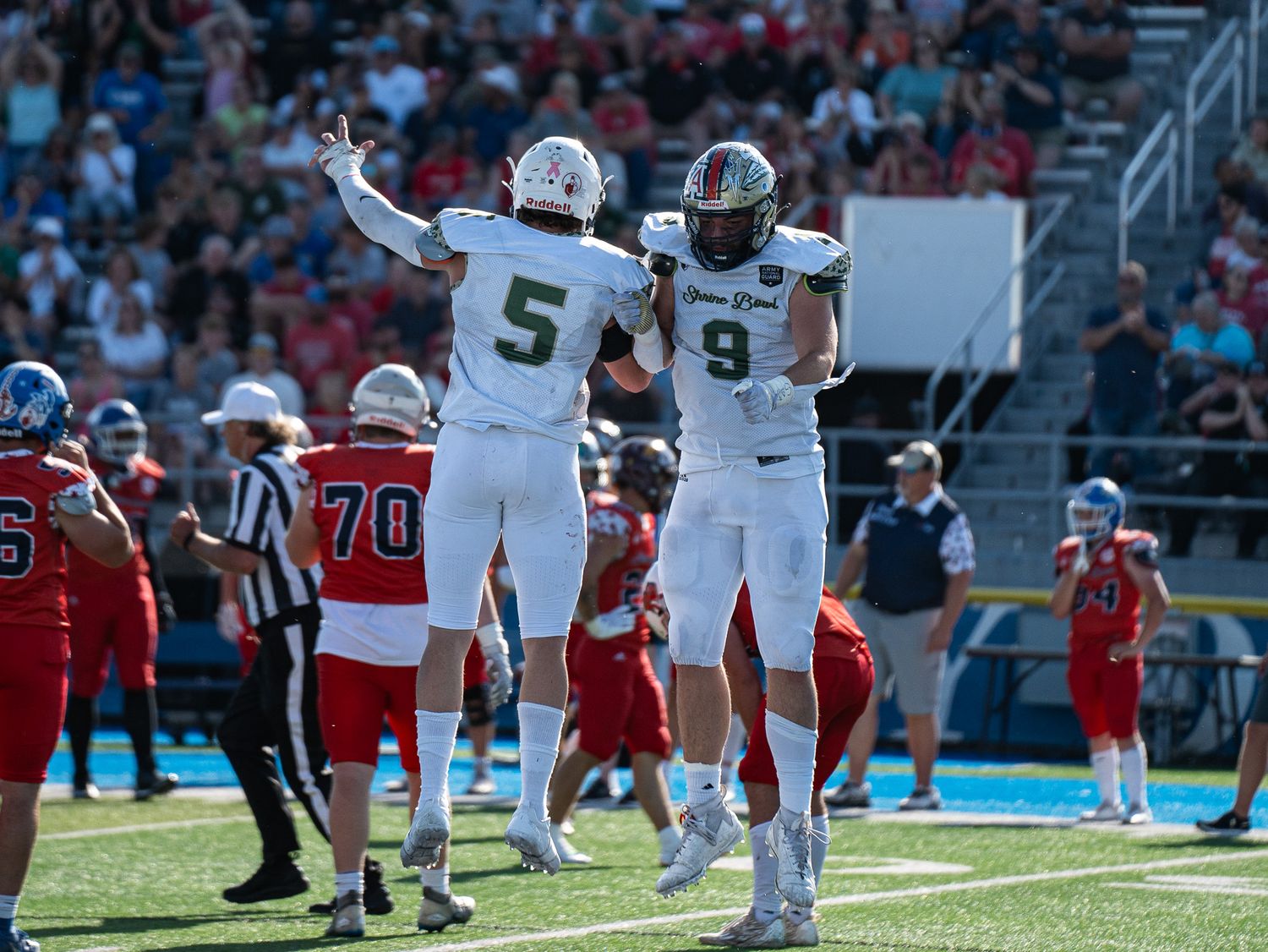 Two football players in white uniforms celebrate with a mid-air celebration.