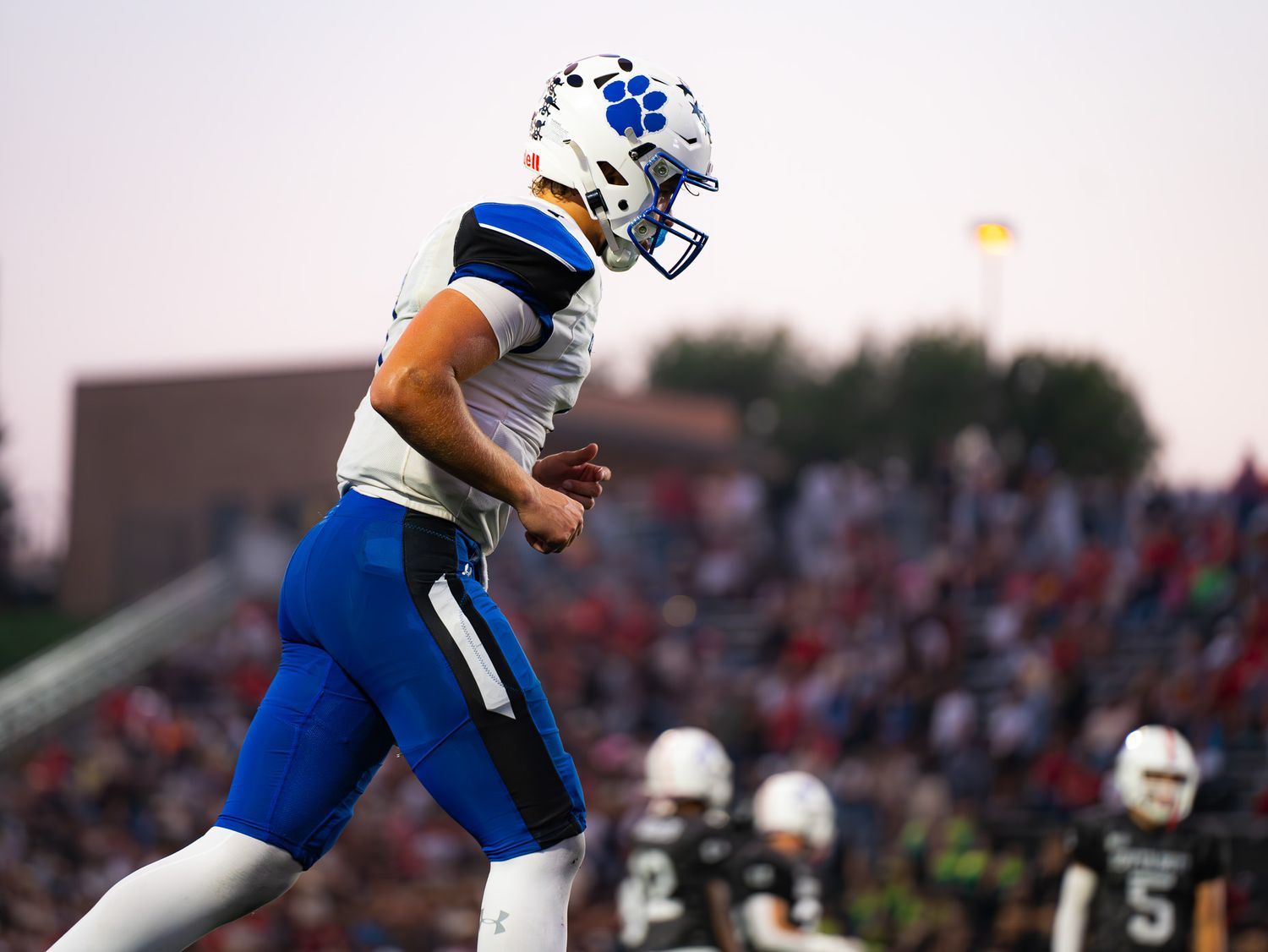 Football player in blue uniform runs during sunset game.