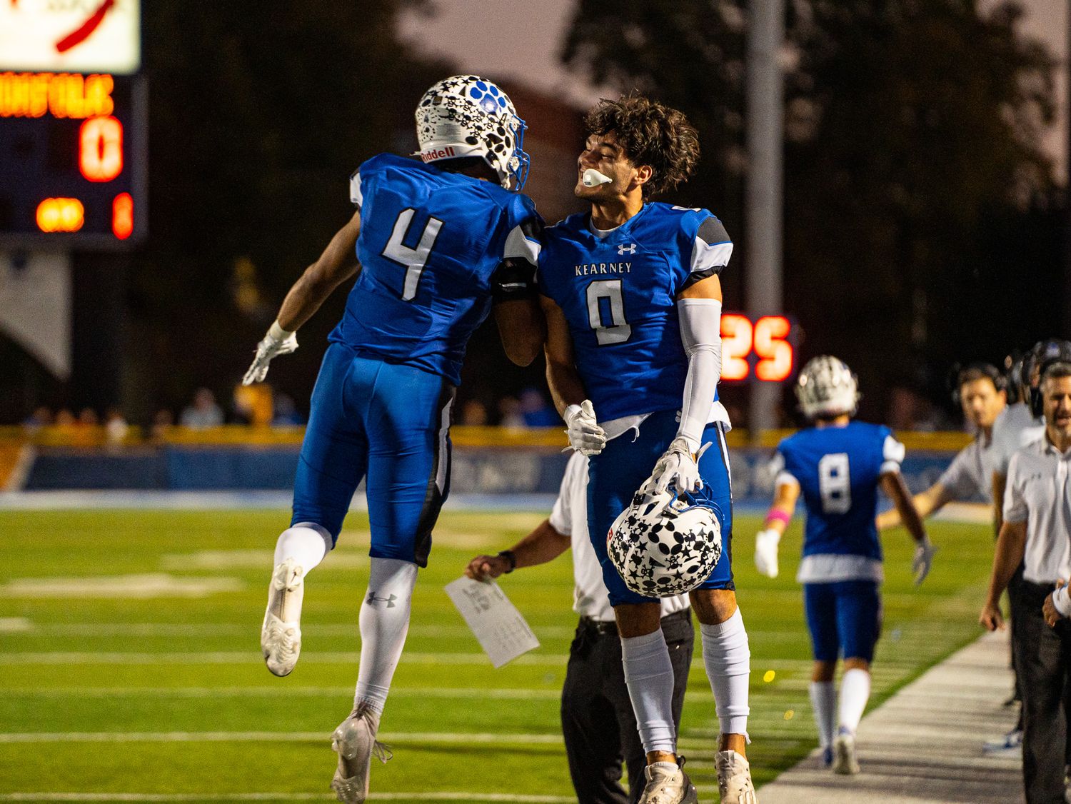 Players celebrate with energetic sideline celebration during nighttime football game.