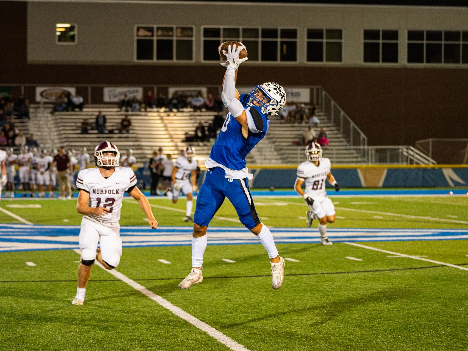 Player leaps high to catch football in end zone during night game.