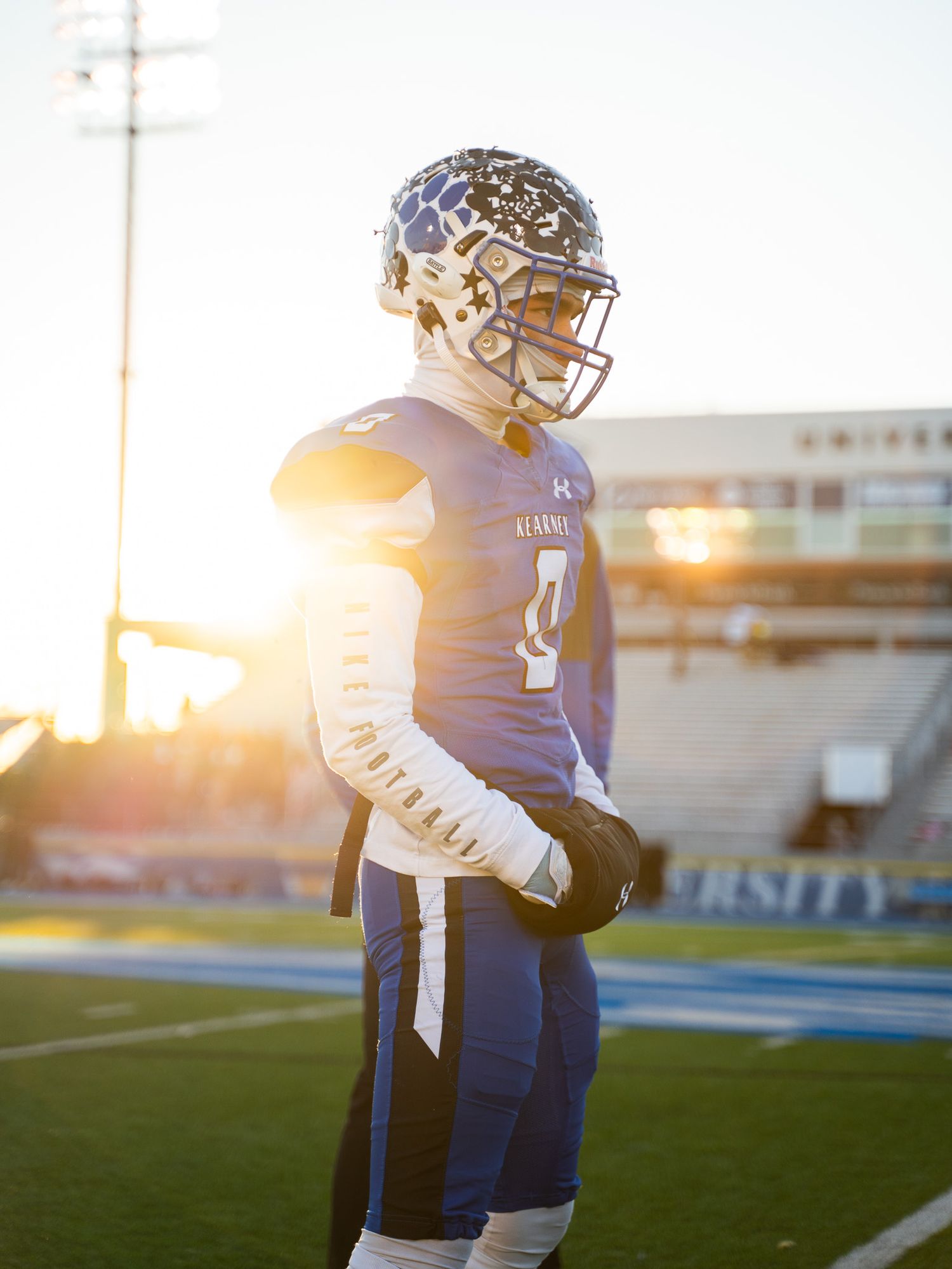 Football player stands silhouetted against sunset on field.