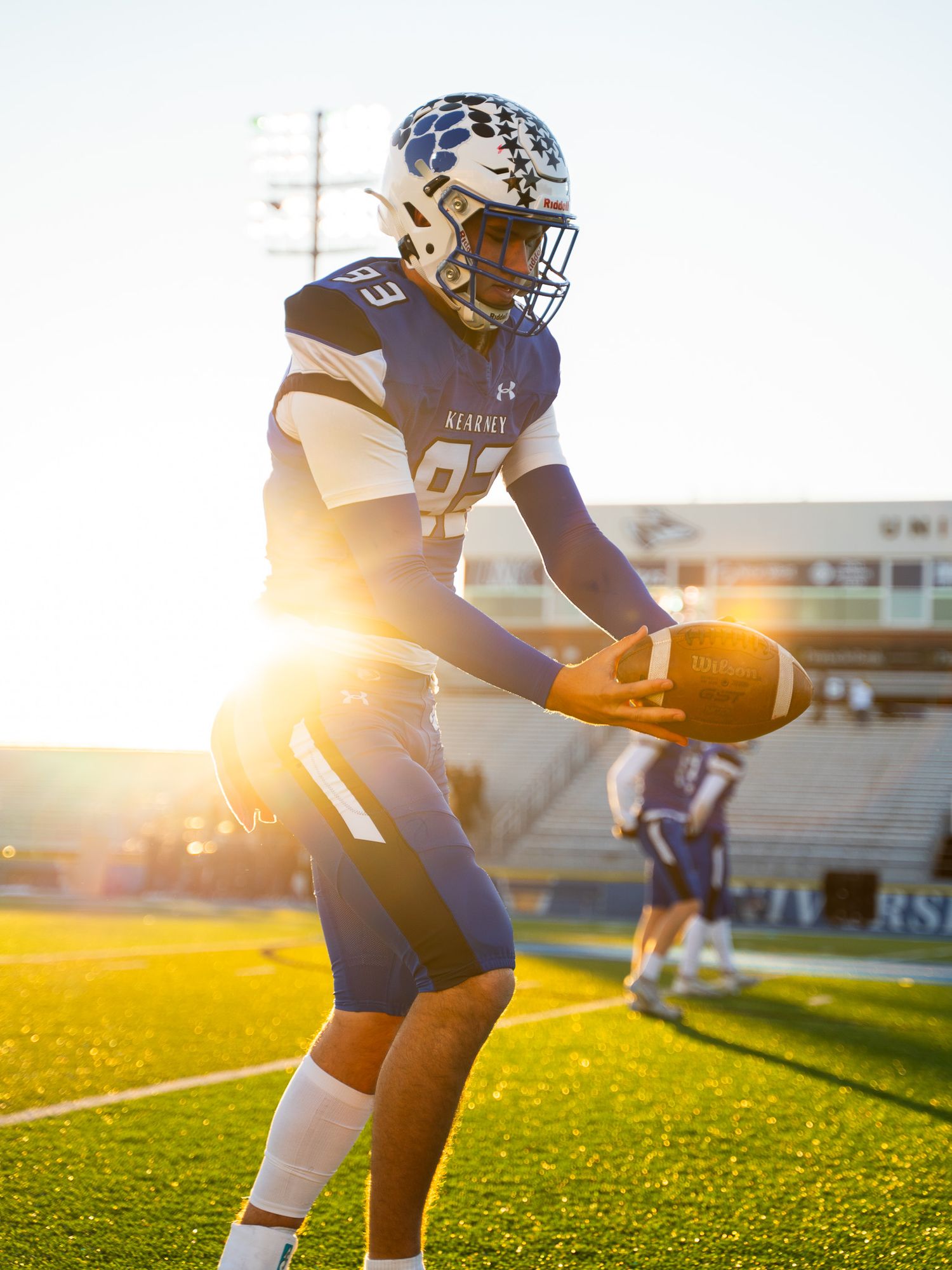 Football player in navy uniform catches ball during sunset practice at stadium.