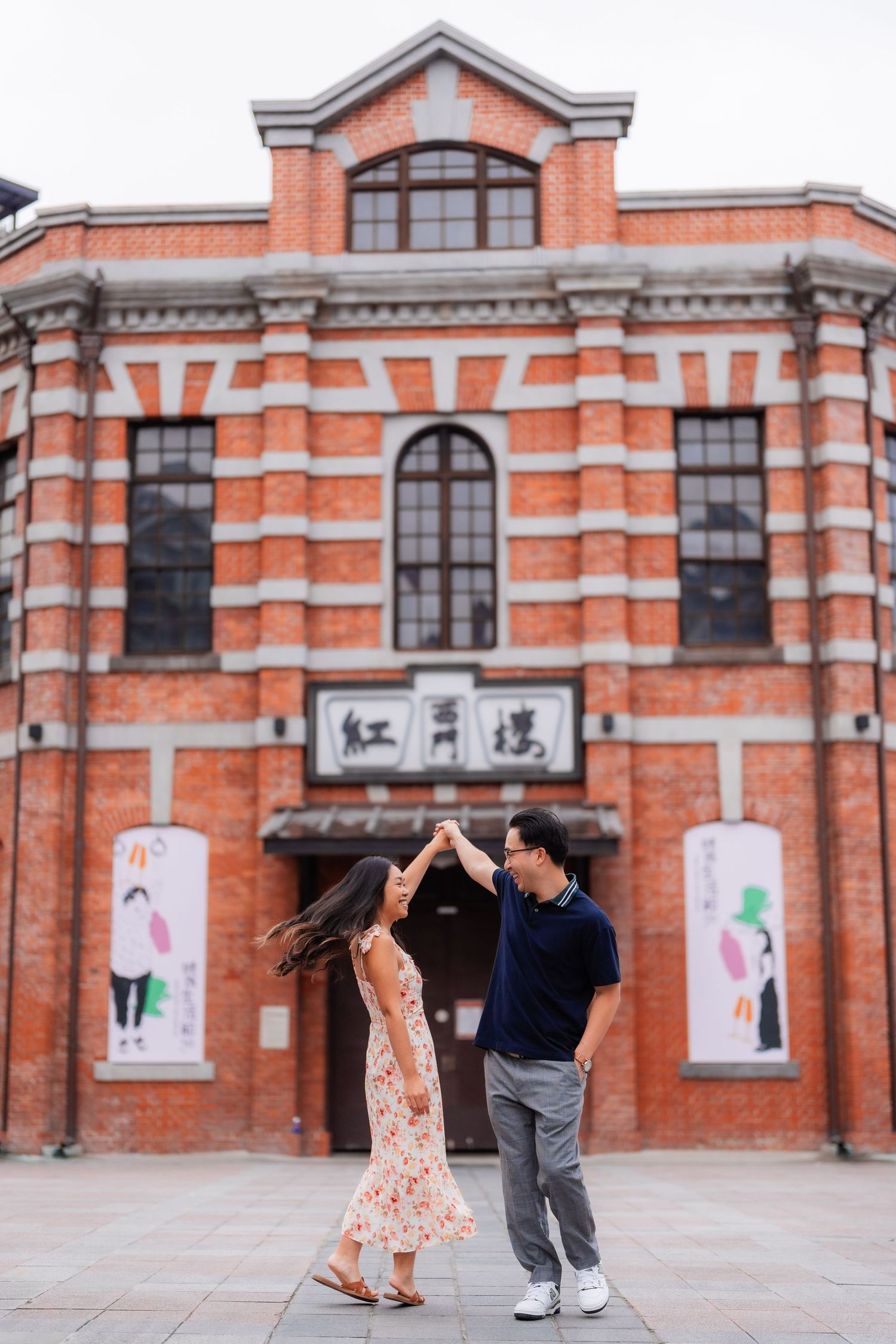 A couple dancing in front of a historic red brick building with Chinese characters in Taiwan.