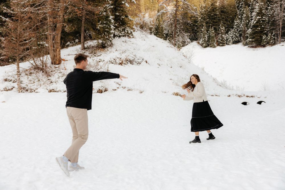 Joyful couple playing in the snow with outstretched arms in a winter forest setting.