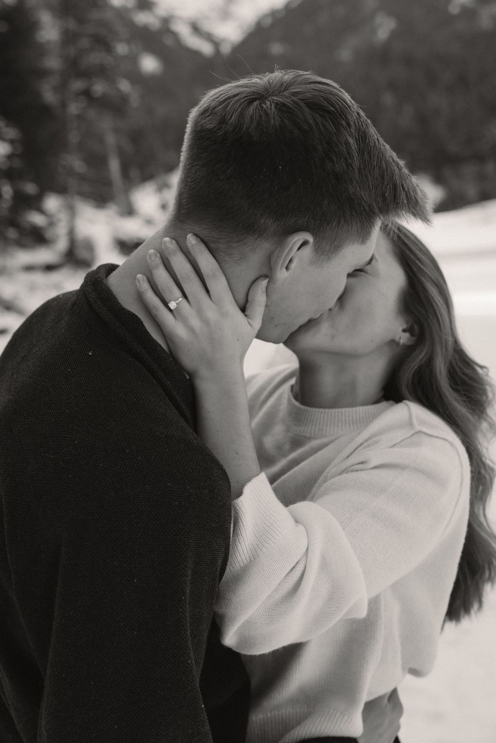 Black and white close-up of an engaged couple kissing, showing engagement ring on hand.